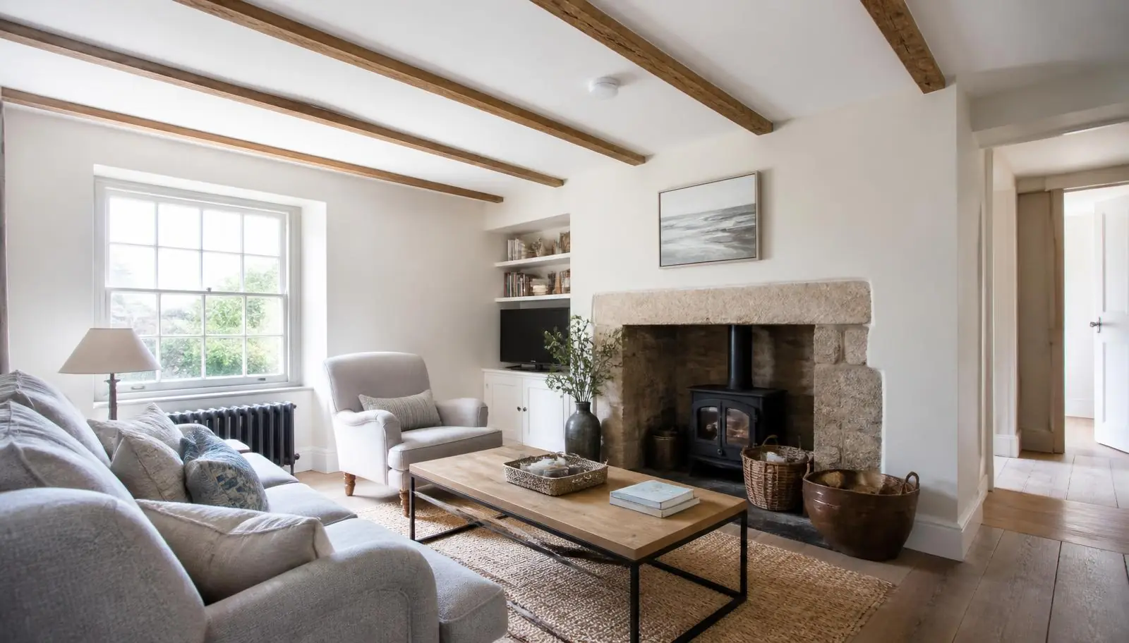 Bright British holiday cottage living room with exposed beams, wood burner and a ceiling smoke alarm